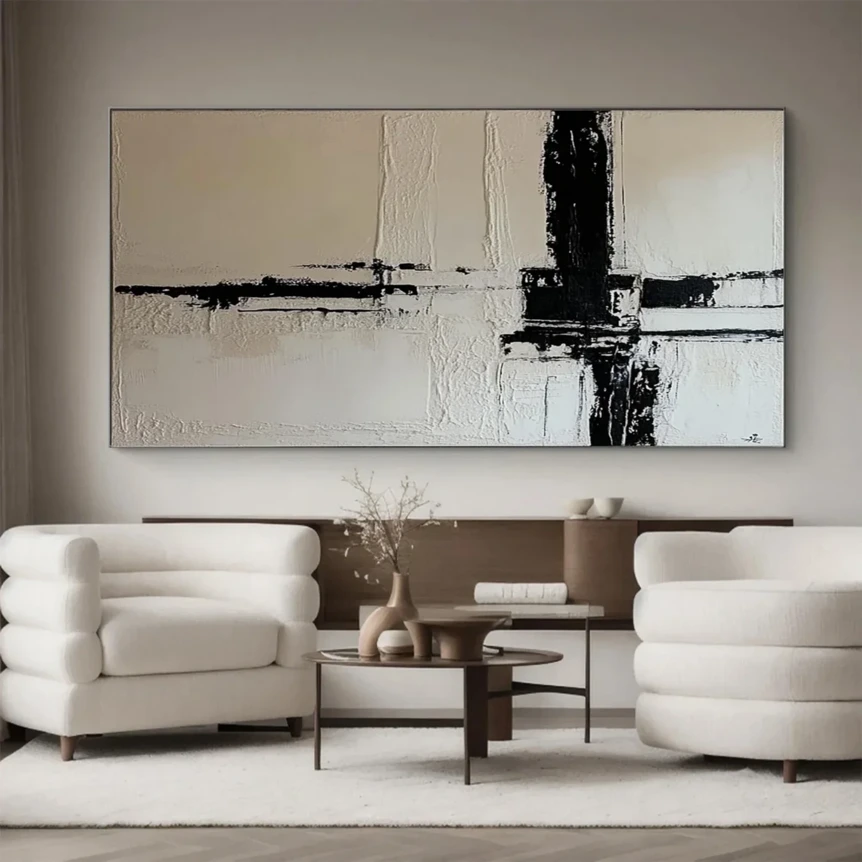 Large abstract black and white painting above two cream armchairs with modern coffee table in neutral living room