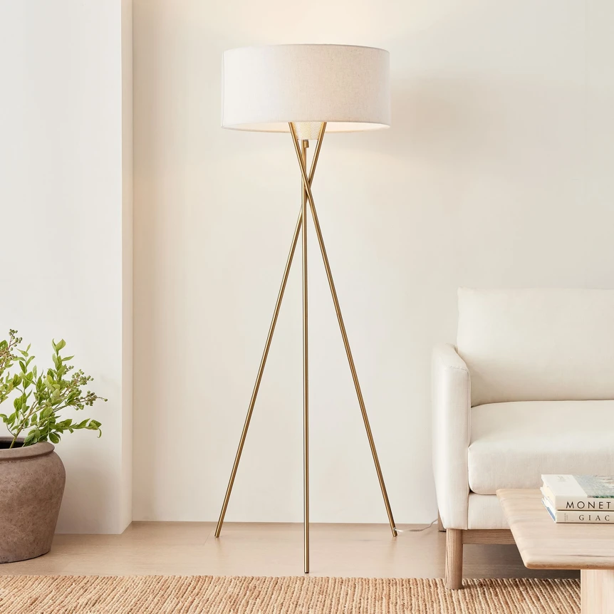 Modern tripod floor lamp with white drum shade next to white sofa in contemporary living room