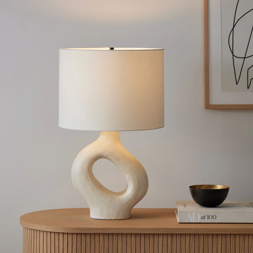 Modern sculptural table lamp with cream shade on wooden credenza in minimalist living room setting