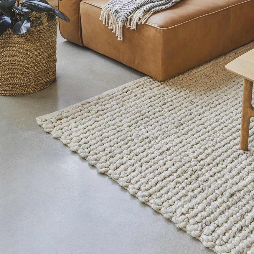 Modern textured cream area rug on gray floor next to tan leather ottoman and woven basket