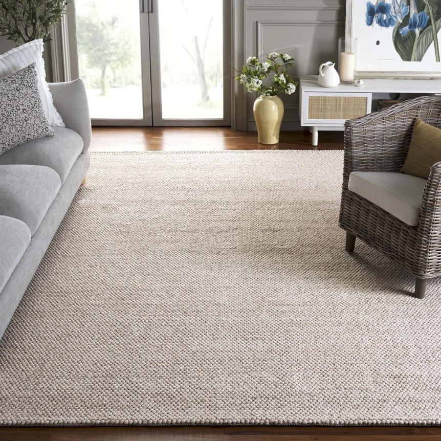 Large beige textured area rug in modern living room with gray sofa and wicker chair
