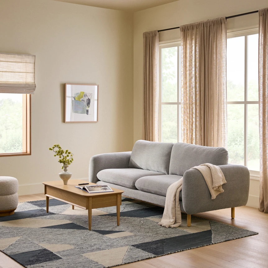 Modern gray sofa with wooden coffee table in minimalist living room with natural light and neutral decor