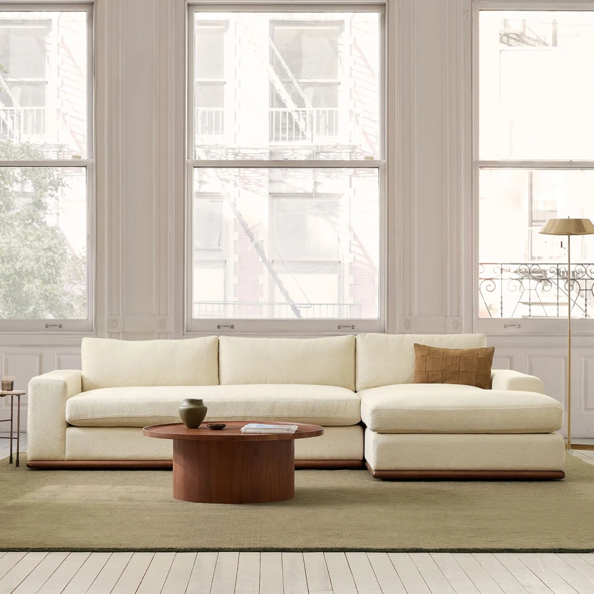 Modern cream sectional sofa with chaise and wood coffee table in bright minimalist living room with large windows