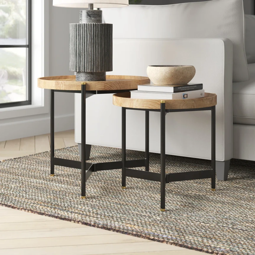 Modern nesting side tables with round wood tops and black metal legs in contemporary living room setting