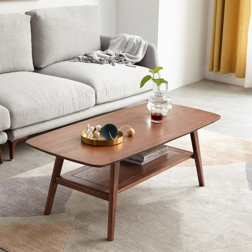 Mid-century modern wooden coffee table with lower shelf in bright living room with gray sofa and natural light