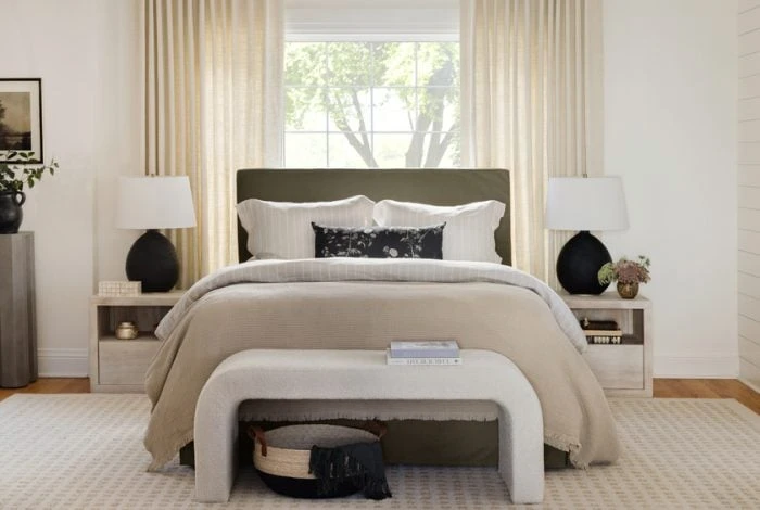 Modern bedroom with neutral tones, upholstered headboard, white bedding, wooden nightstands, and natural light