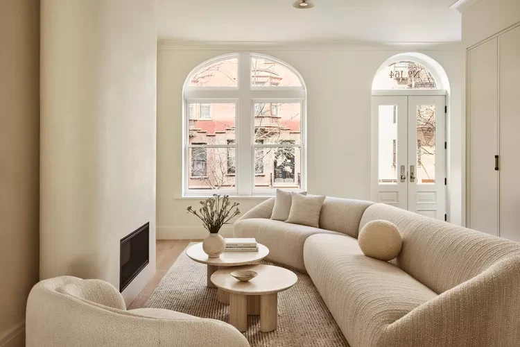 Bright Scandinavian living room with curved beige sofa, round coffee table, and arched windows with neutral tones