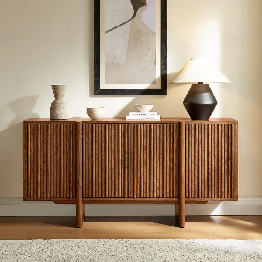 Mid-century modern wood sideboard with fluted doors displaying decorative vases and lamp in minimalist living room