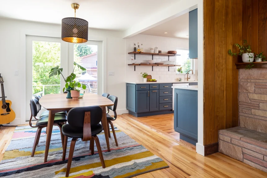 Mid-century modern dining room with blue kitchen cabinets, wood floors, yellow striped rug, and pendant lighting