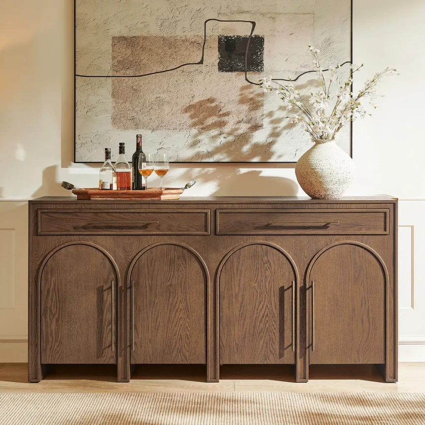 Wooden sideboard with arched door panels displaying decorative items and abstract artwork in neutral-toned dining room