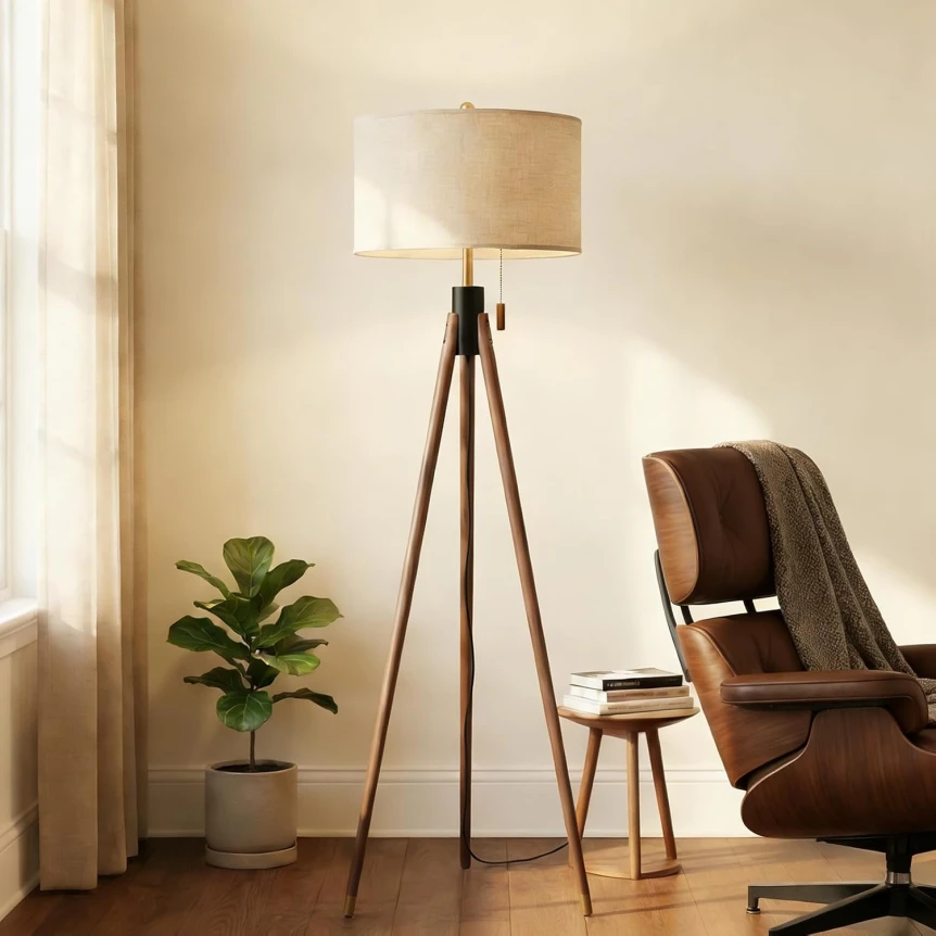 Mid-century modern tripod floor lamp with wooden legs and beige shade beside brown leather chair in living room