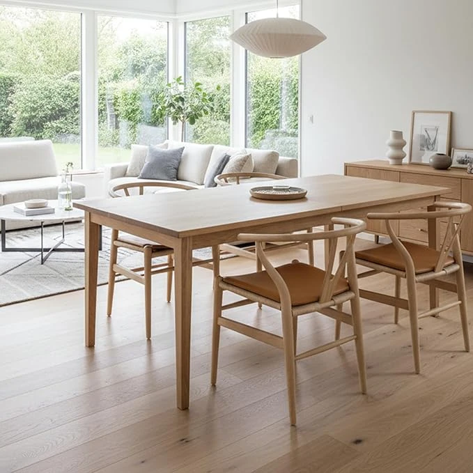 Light wood Scandinavian dining table with matching chairs in bright living space with white sofa and large windows