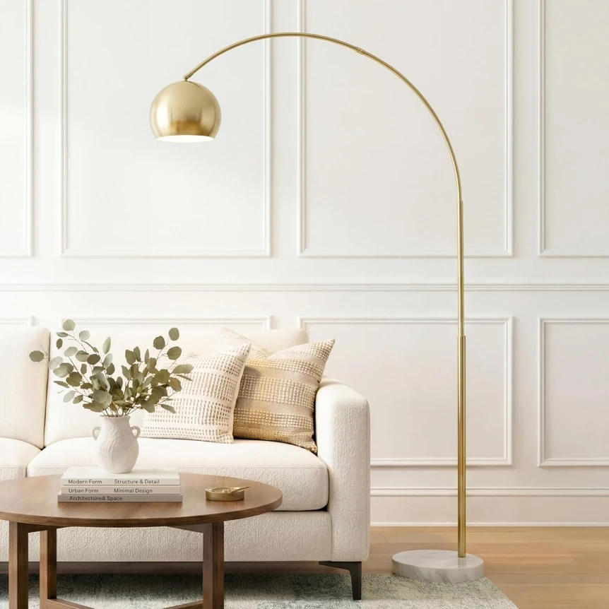 Gold arc floor lamp with dome shade beside white sofa in modern living room with marble base