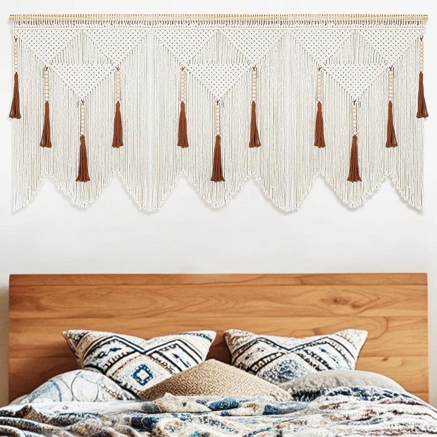 Macrame wall hanging with geometric patterns and tassels above wooden headboard with patterned pillows