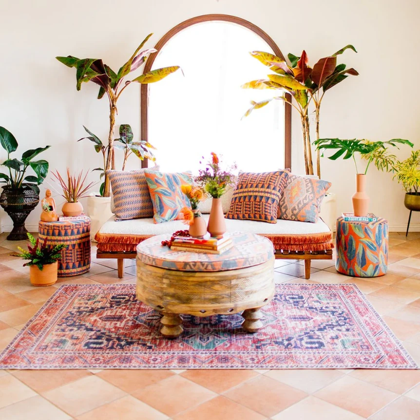 Bohemian living room with patterned rug, low seating, tropical plants, and circular arch backdrop