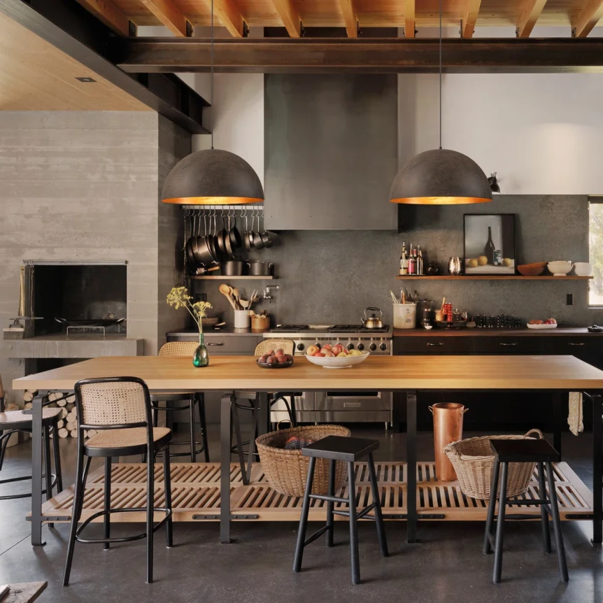 Modern industrial kitchen with concrete walls, exposed beams, black pendant lights, and wooden dining table