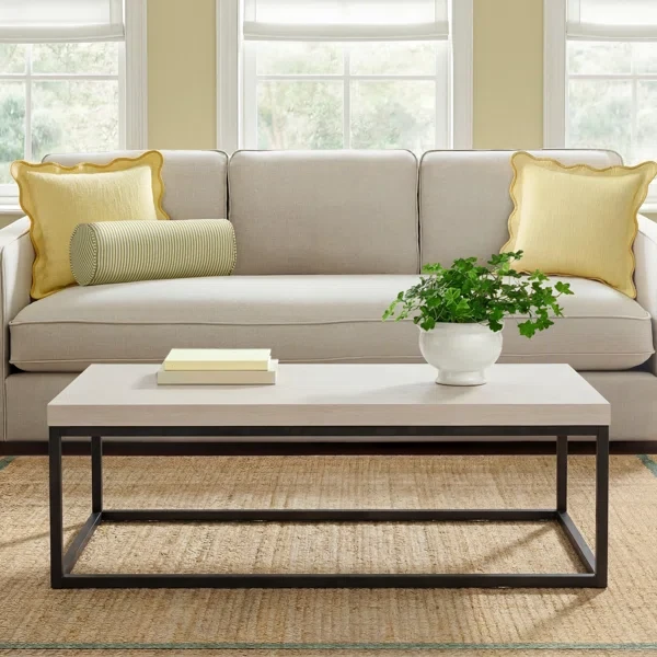 Modern white marble coffee table with black metal frame in living room with beige sofa and yellow pillows