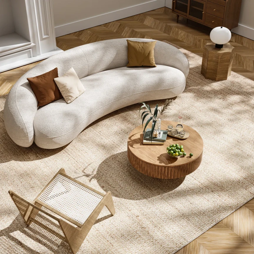 Modern curved white sofa with brown pillows, round wooden coffee table, and neutral area rug in sunlit living room