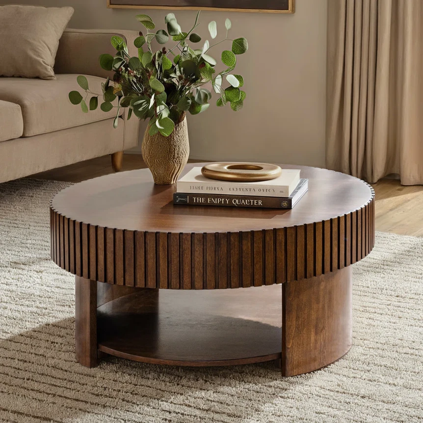 Round wooden coffee table with ribbed base and white marble top styled with vase and books in modern living room