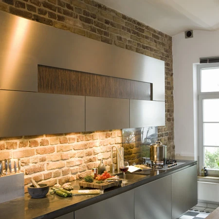 Industrial kitchen with exposed brick backsplash, sleek cabinets, and black countertops creating bold modern design