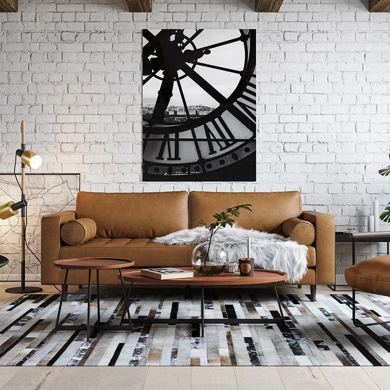 Industrial living room with tan leather sofa, white brick wall, clock art, and striped rug in modern loft space