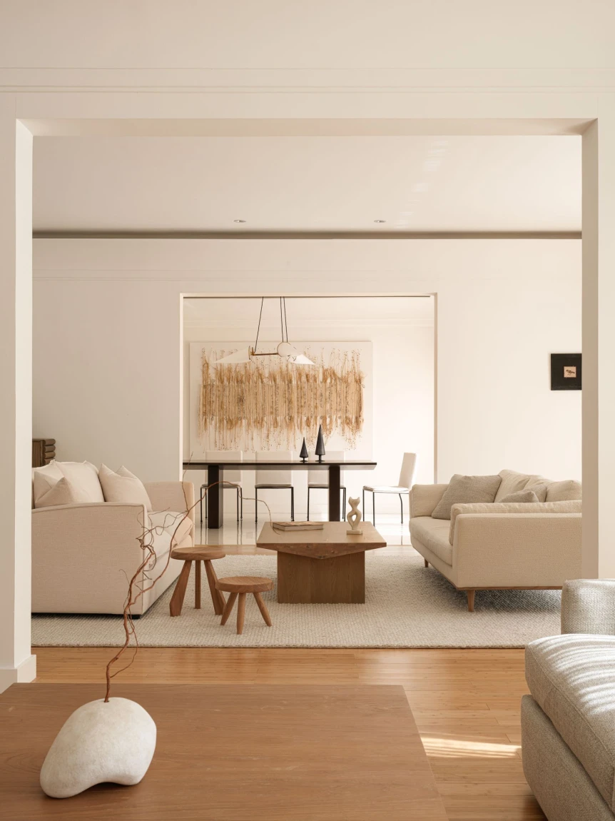 Warm minimalist living room with cream sofas, natural wood coffee table, and beige textured chandelier