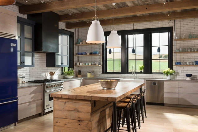 Industrial kitchen with exposed wooden beams, reclaimed wood island, white subway tile backsplash, and black-framed windows
