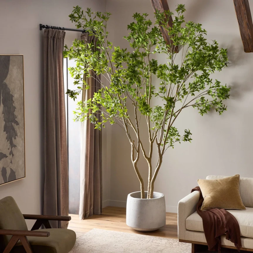 Large potted artificial tree with green leaves in modern living room with neutral decor and brown curtains