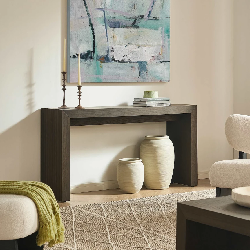 Dark wood console table with decorative vases underneath in modern entryway with abstract artwork and neutral decor