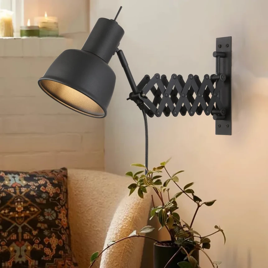 Black scissor arm wall lamp with adjustable accordion mount extending over bedroom nightstand with plant