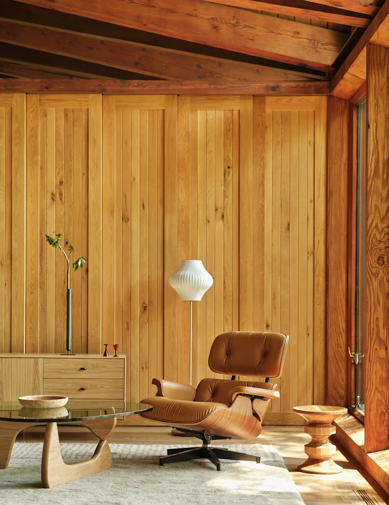 Mid-century modern living room with tan leather lounge chair, wood paneling, and exposed beam ceiling