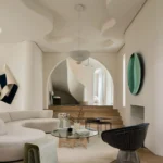 Warm minimalist living room with curved white sofa, natural wood flooring, sculptural lighting, and organic textural elements