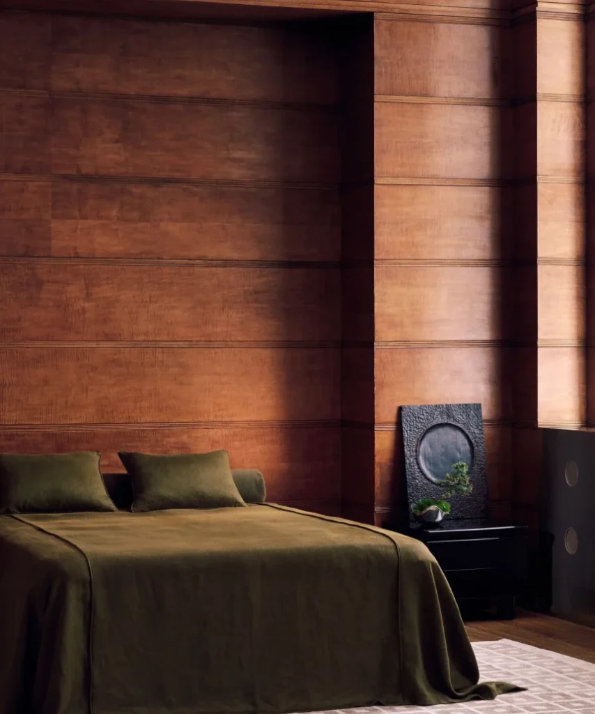 Minimalist bedroom with wooden paneled walls, olive green bedding, and modern black nightstand showcasing Japandi design s...