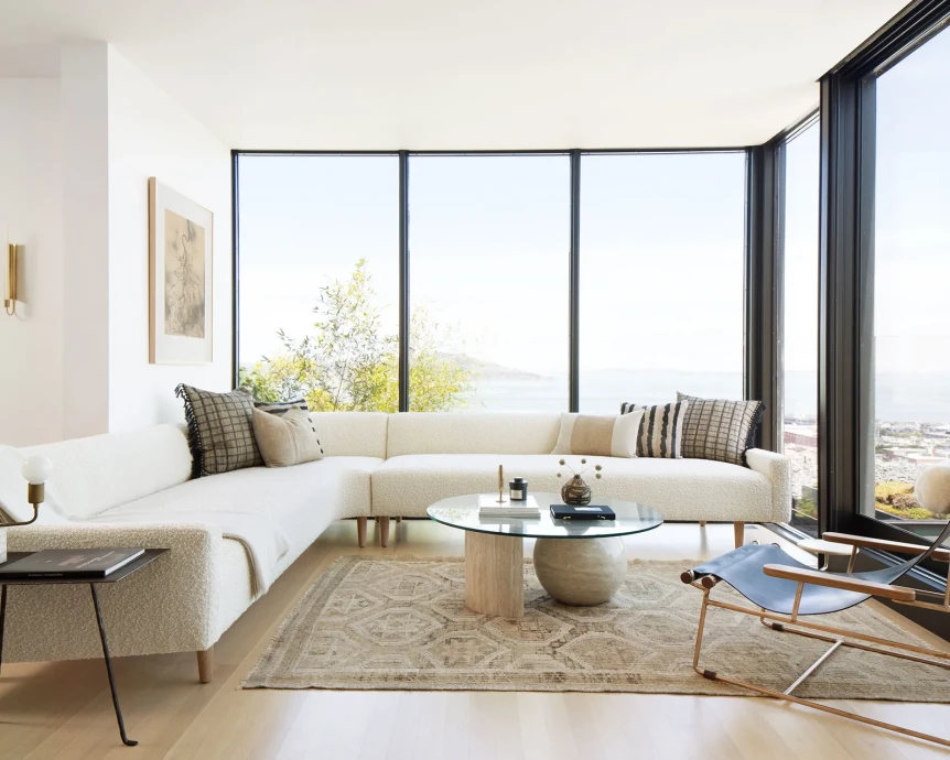 Bright Scandinavian living room with white curved sofa, natural jute rug, and large windows overlooking city views