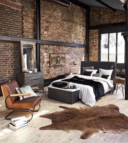 A chic modern industrial bedroom with exposed metal brick walls upholstered furniture a chest for storage and some animal skin rugs