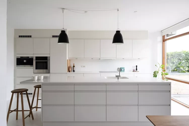 Modern Scandinavian kitchen with white cabinetry, minimalist island, black pendant lights, and natural light from large wi...
