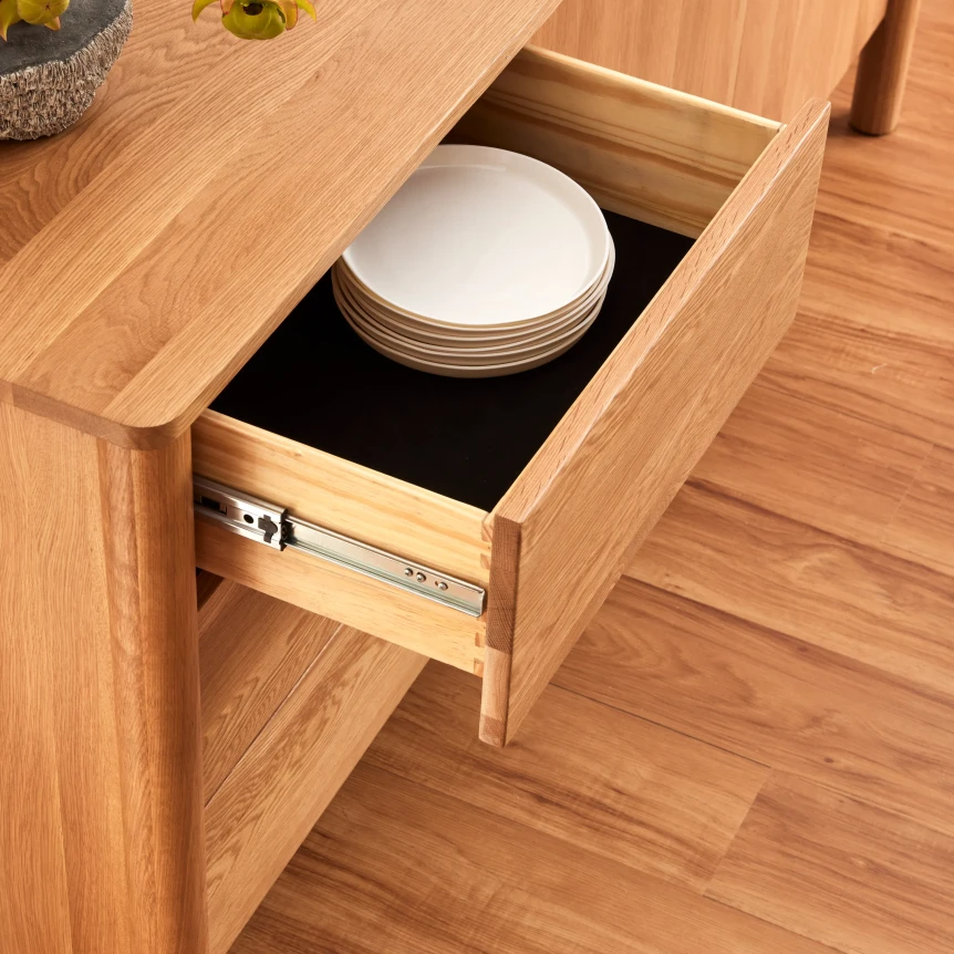 Open wooden sideboard drawer with white plates on smooth-glide rails showcasing storage functionality