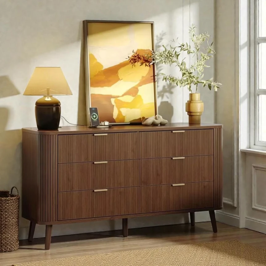 Mid-century modern wooden dresser with drawers, decorative lamps, artwork, and plants in warm-toned bedroom