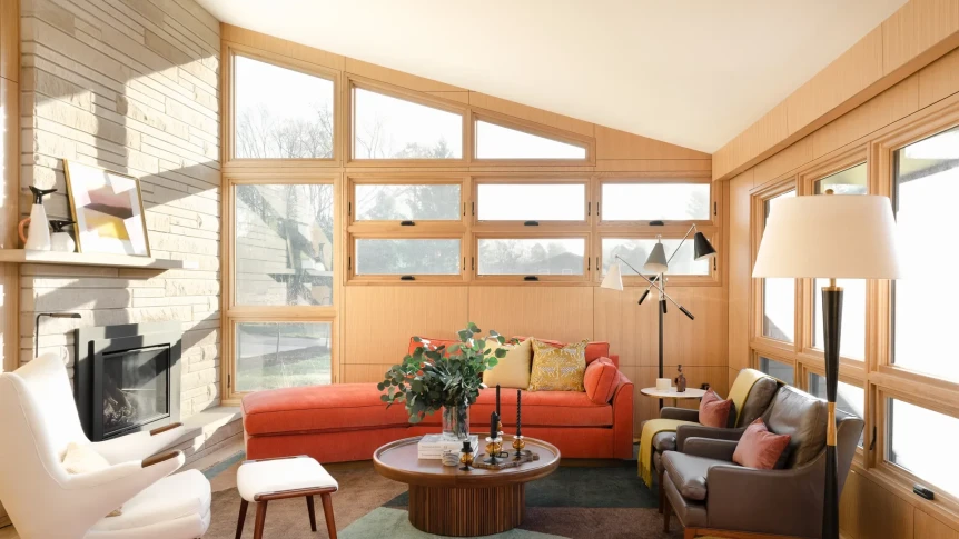 Mid-century modern living room with exposed wooden beams, orange sofa, and large windows with natural light