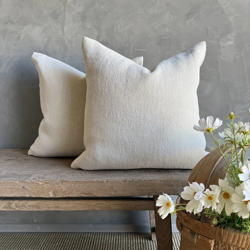 Neutral linen throw pillows on rustic wooden bench with white flowers and gray concrete wall background