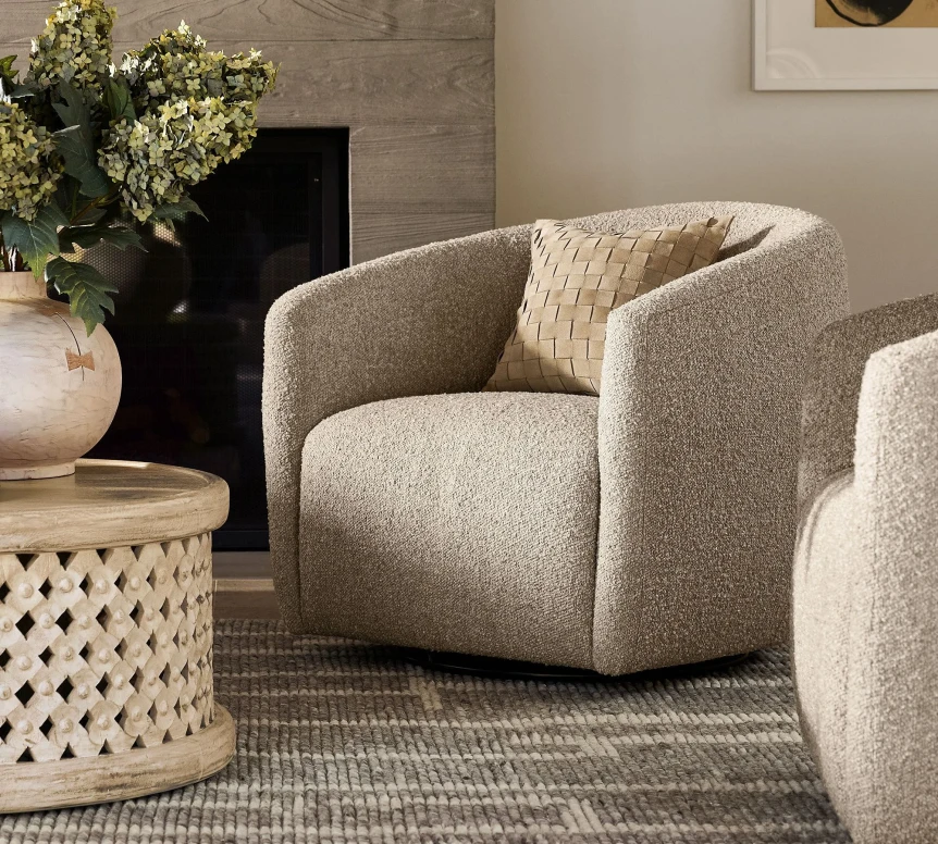 Modern beige curved armchair with decorative pillow next to carved wooden side table in neutral living room