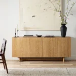 Modern oak sideboard with minimalist decor including black vase, candles, and abstract art in neutral living room