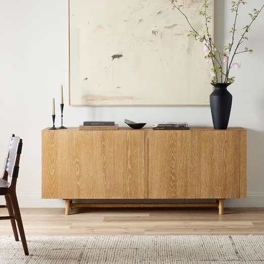 Modern oak sideboard with minimalist decor including black vase, candles, and abstract art in neutral living room