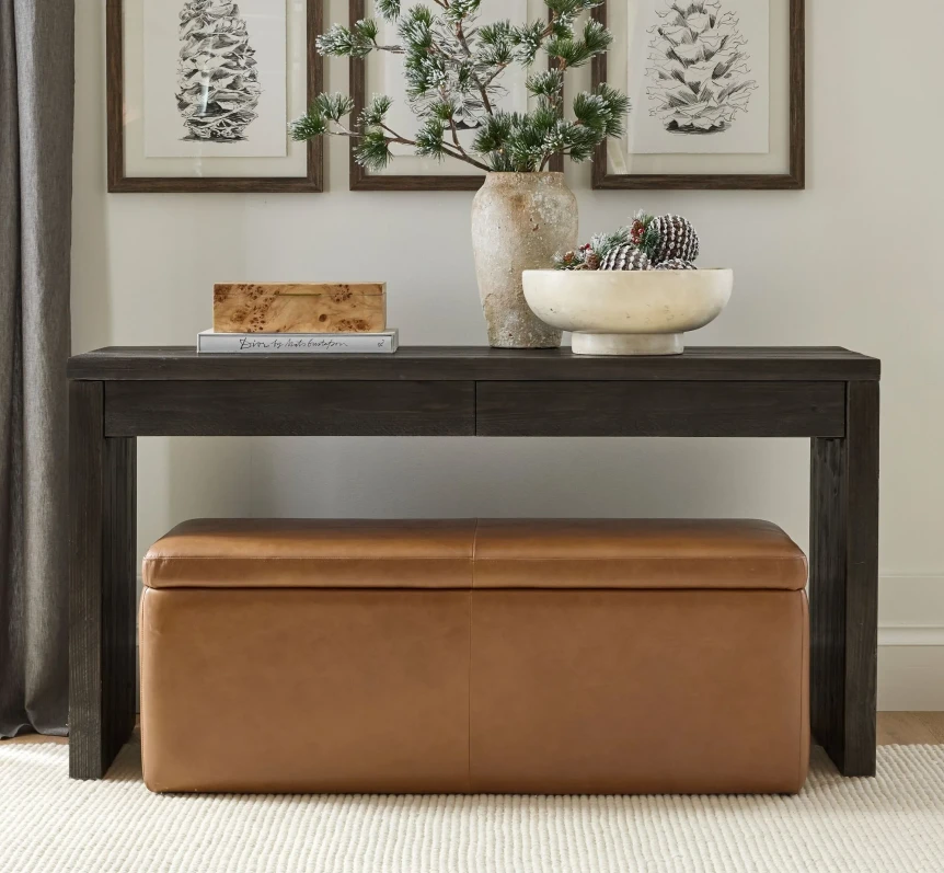 Modern storage bench in tan leather tucked under black console table with decorative items on top