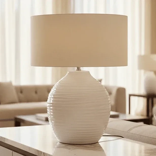 White ceramic table lamp with beige drum shade on living room coffee table