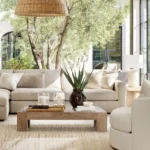 Bright modern living room with neutral beige sofa, wooden coffee table, and large windows overlooking garden