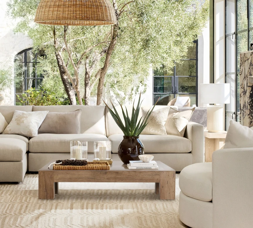 Bright modern living room with neutral beige sofa, wooden coffee table, and large windows overlooking garden