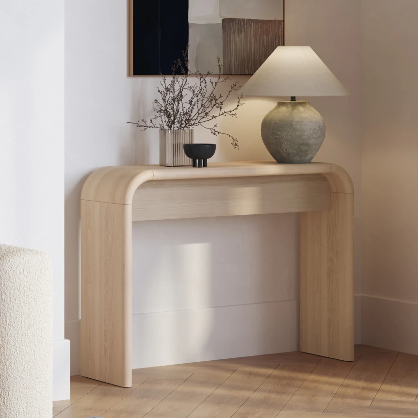 Modern curved wood console table with lamp and decor in minimalist entryway setting