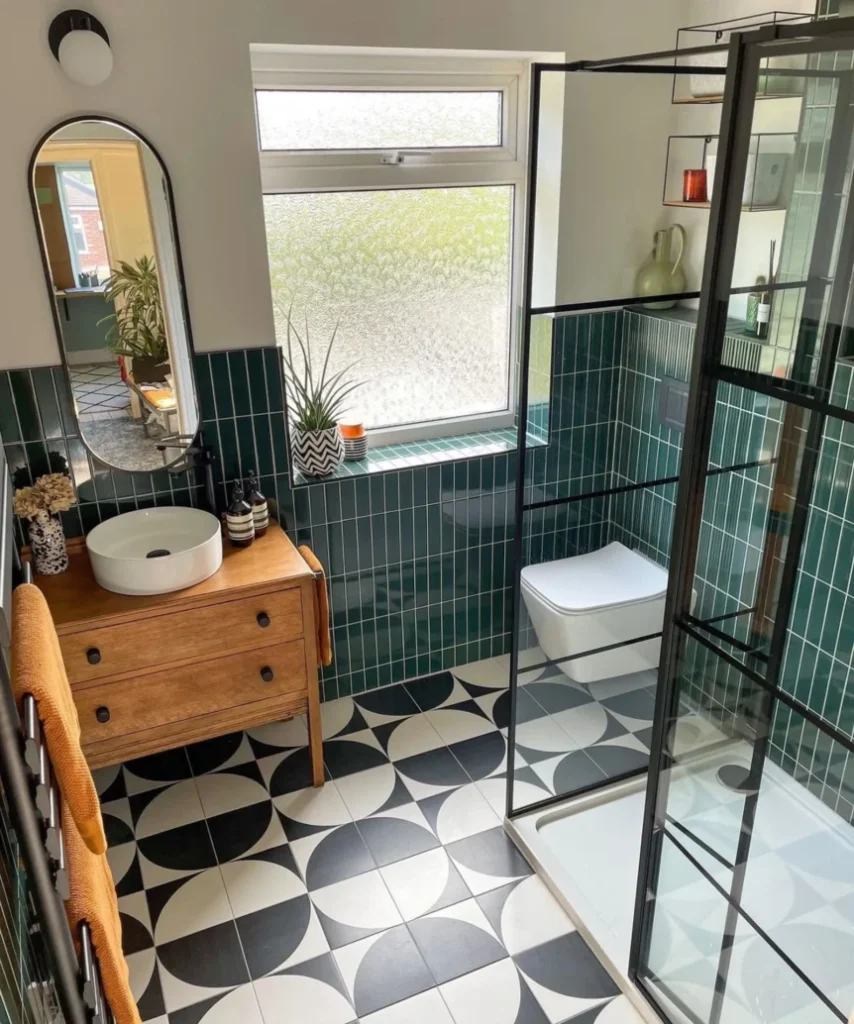 Modern Scandi bathroom with green subway tiles, geometric floor, wooden vanity, black-framed glass shower, and arched mirror