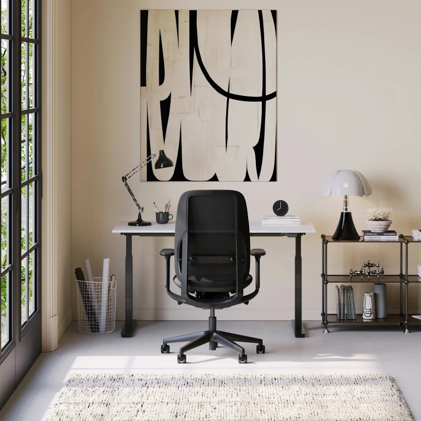 Modern minimalist home office with black ergonomic chair, simple desk, and abstract wall art in neutral tones